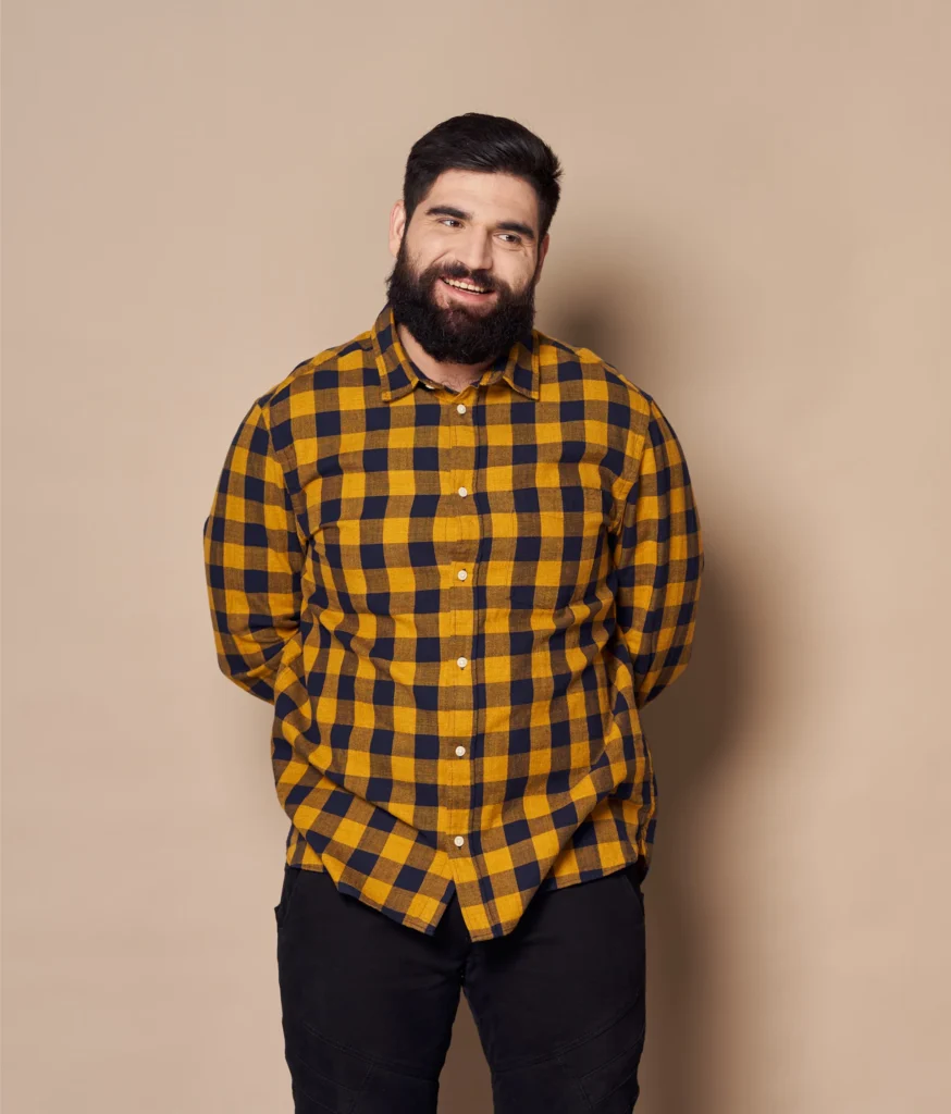 Portrait of a smiling man with a beard wearing a yellow and navy blue plaid shirt.