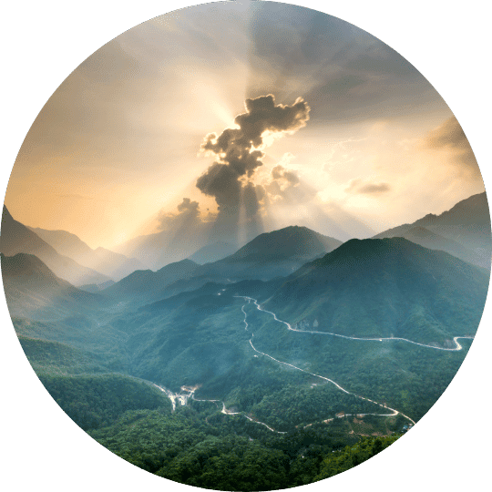A circular image of mountains and valleys with a winding road and sun rays breaking through the clouds.